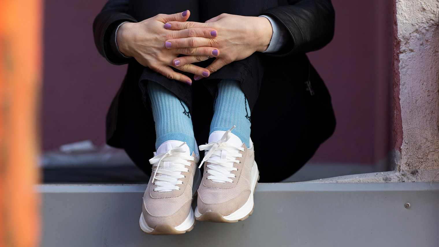 Nainen istuu lastauslaiturilla lenkkarit jalassa kädet ristissä. 