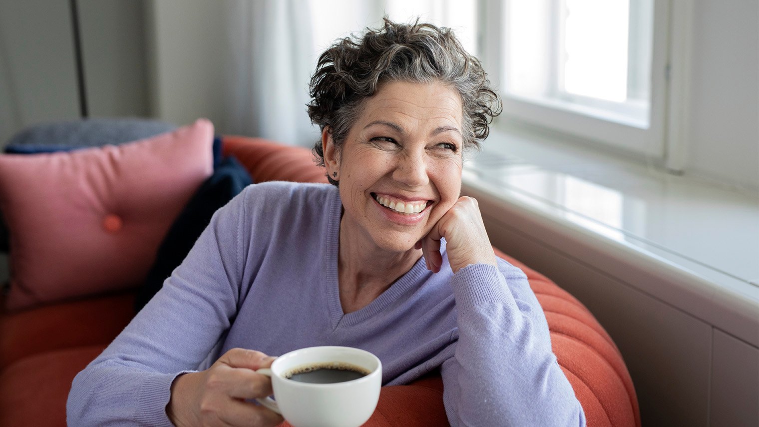 Nainen istuu sohvalla kahvikuppi kädessään.
