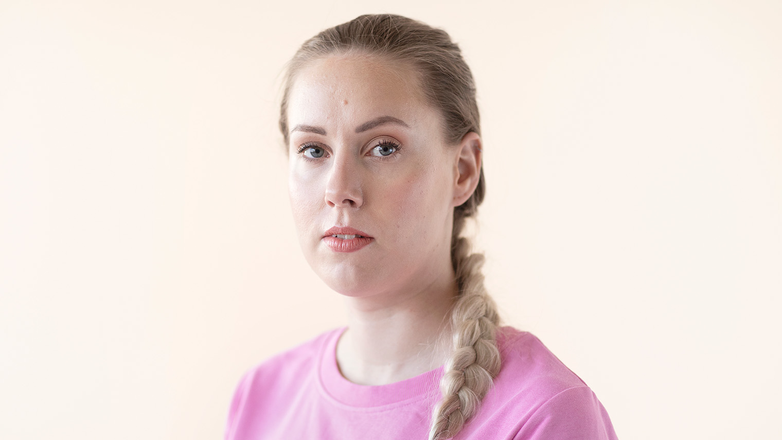 Vaaleahiuksinen lettipäinen nainen vaaleanpunainen paita päällään.