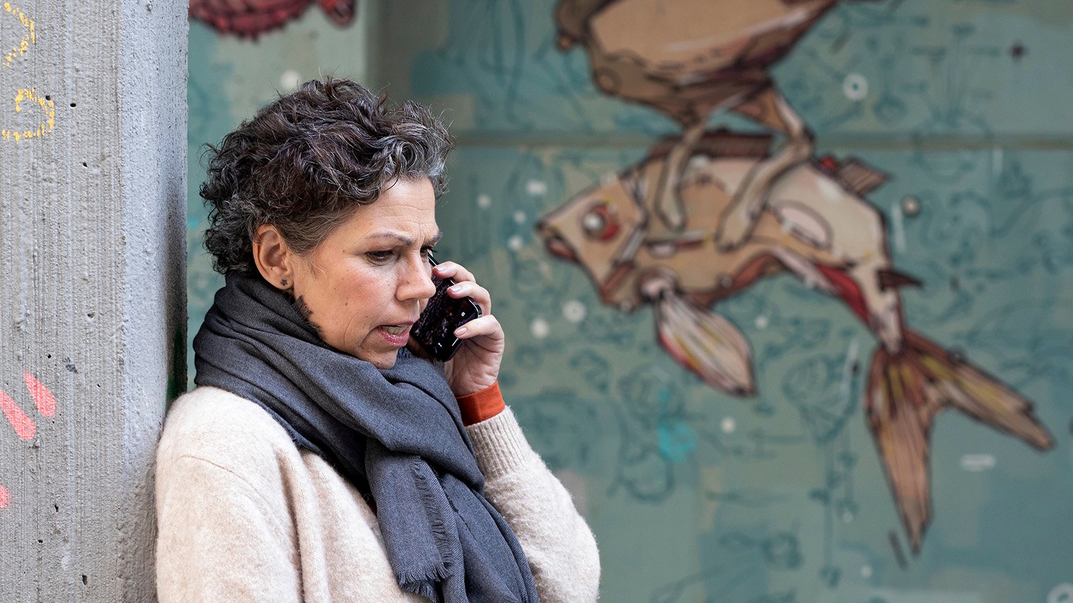 Vakava nainen puhuu kännykkään graffitiseinän edessä.