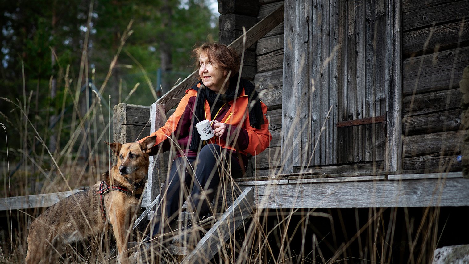 Marja-liisa Honkasalo mökin edessä koiransa kanssa.